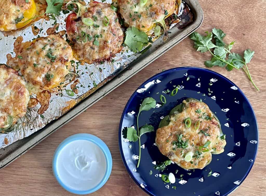 A plate and tray of chorizo-stuffed peppers topped with melted cheese, cilantro, and green onions with a side dish of sour cream