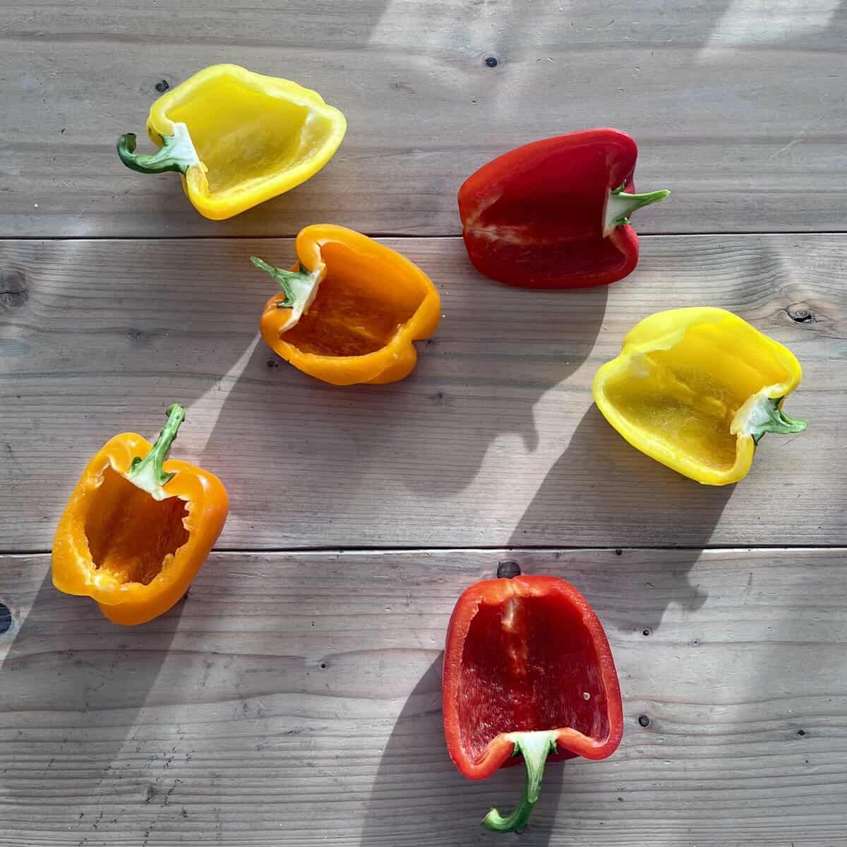 Red, yellow, and orange hollow bell pepper halves on a table