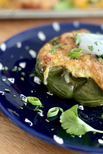 Roasted green bell pepper on a blue plate topped with melted cheese and sour cream