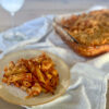 A plate of chicken pasta in tomato sauce with breadcrumb streusel and a casserole dish