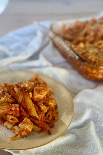 A plate of chicken pasta in tomato sauce with breadcrumb streusel and a casserole dish