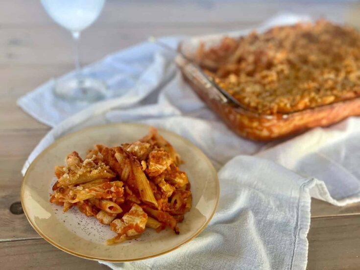 A plate of chicken pasta in tomato sauce with breadcrumb streusel and a casserole dish