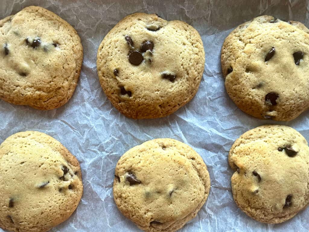 Chocolate chip cookies with somewhat browned edges and light, shiny centers on parchment 